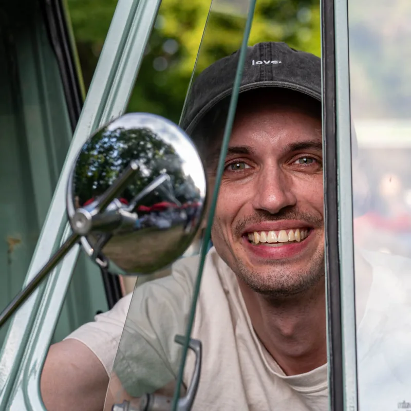 Joshua, Co-Founder der alveare food GmbH, lacht aus dem Fenster der Ape